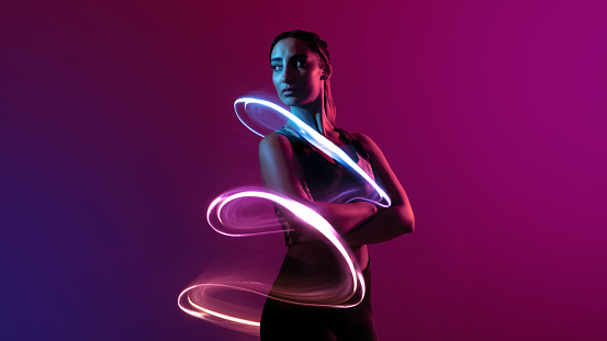 Three-quarter-length studio portrait of a young female model standing with her arms crossed looking away from the camera. The image has been manipulated in post-production with a futuristic lighting pattern surrounding her.