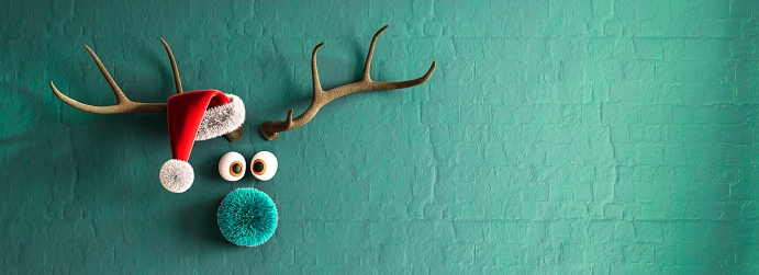 Reindeer with red nose and Santa hat on vibrant turquoise blue wall background with copy space. 3D Rendering, 3D Illustration
