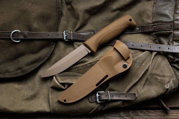 istock Modern knife with rubberized handle and plastic sheath. Cold steel lies on a vintage hiking backpack. Wooden background. 1673660083