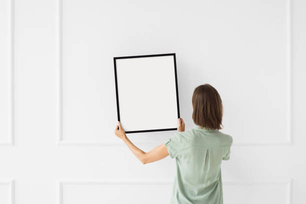 istock Woman holding blank picture frame against a wall. Artwork mock-up concept 1673691298