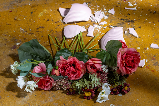 Broken vase of fake flowers on floor.