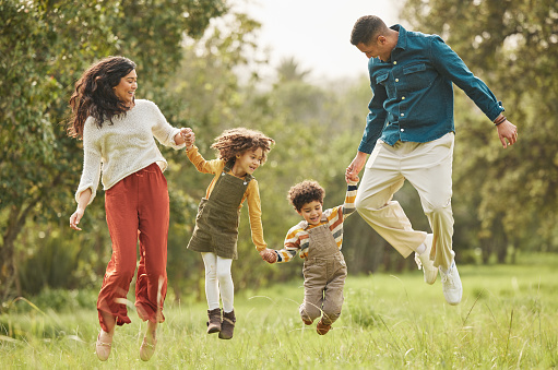 Holding hands, park and parents jump with children in nature for playing, bonding and fun together in field. Happy family, mother and father with kids outdoors on holiday, adventure and vacation