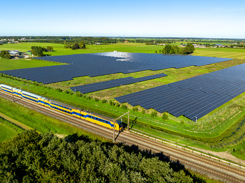 Train of the Nederlandse Spoorwegen NS (Dutch Railways) driving past a field of solar panels near Zwolle in Overijssel, Netherlands during a sunny day in summer.