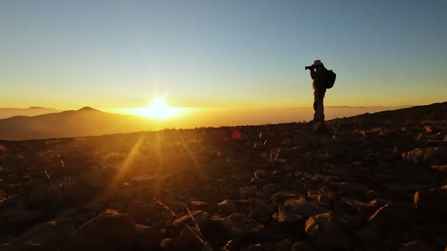 Silhouette of a photographer man who is shooting photos with dslr camera while watching  sunrise on the top of a mountain