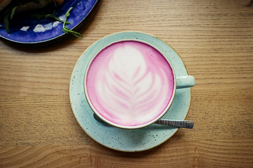 Cup of pink cappuccino in blue cup on wooden  table in a cafe closeup, top view