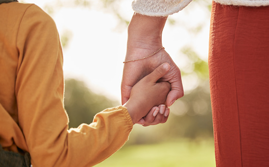 Close-up of mother, father and their toddler holding hands together in the park.