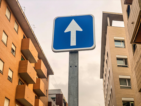 Low angle view of traffic sign with arrow pointing up in front of residential buildings