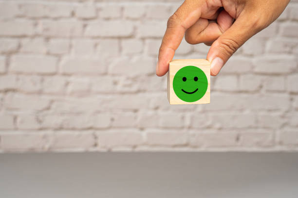 istock Positive feedback concept. Hand holding a green happy mood icon on a white brick wall background 1673777621