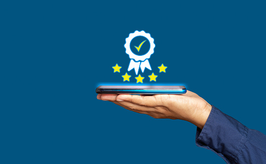 Quality assurance concept. Close-up of a hand businessman holding a smartphone and showing the best quality assurance with five stars symbol for a product, service, and ISO certification