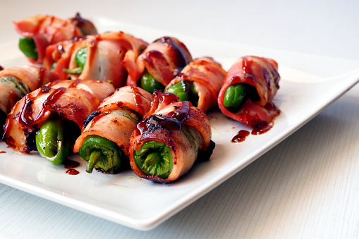 Padron pepper rolls wrapped in bacon on a white plate. Traditional spanish appetizers.