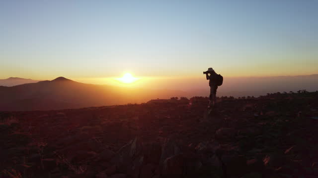 Silhouette of a photographer man who is shooting photos with dslr camera while watching  sunrise on the top of a mountain