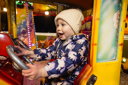 Close up of a little girl playing on a carousel, it's her first time at the funfair​, she is looking at all of the decorations in awe.