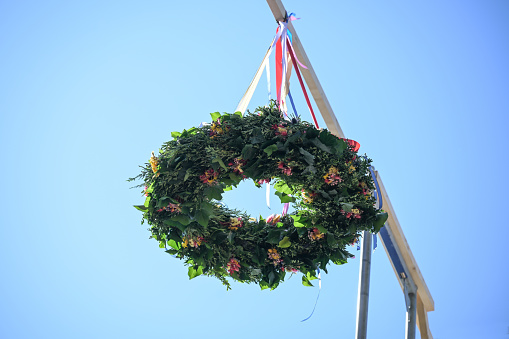 Topping out wreath tied from evergreen branches and flowers hanging with colorful ribbons on a ridge rack in front of a blue sky, copy space, selected focus