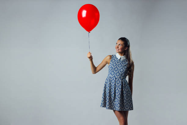 Fashion pretty happy smiling woman in red dress and sunglasses with air balloons heart shape looking up over white background