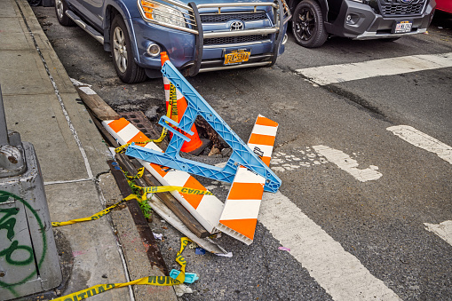 Crescent Street, Long Island City, Queens, New York, USA - August 17th 2023: Pothole at a street corner marked with a overturned barrier and traffic cone