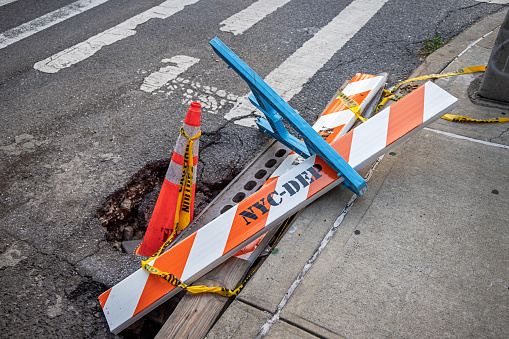 27th Street, Long Island City, Queens, New York, USA - August 11th 2023: Pothole at a street corner marked with a overturned barrier and traffic cone
