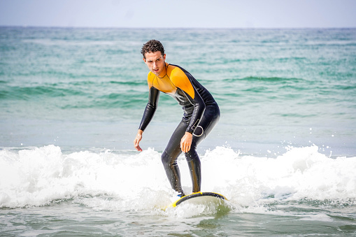 Young Adult Male Surfer with Wetsuit and Face of Concentration Maintaining Balance on his Board While Practicing his Water Sport
