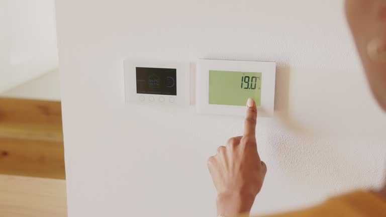 Ethnic woman adjusting smart thermostat control on wall