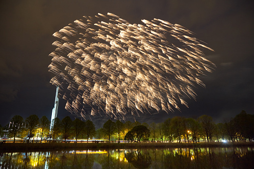 Colorful panoramic view of fireworks over night sky in park near lake.