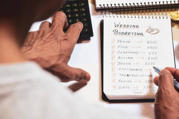 A South Asian man hand calculating the wedding expenses on notepad.