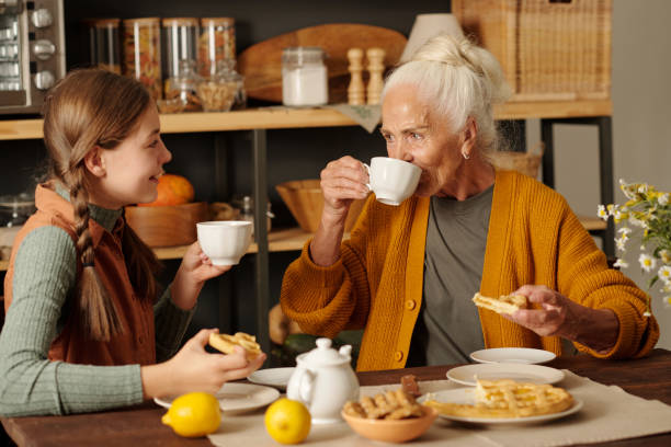 Aged woman with white hair drinking hot herbal tea while sitting by table