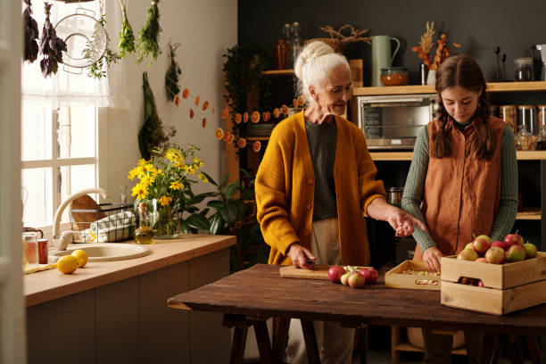 孫娘の隣に立つ白い髪の年配の女性 - grandmother domestic life cooking domestic kitchen ストックフォトと画像