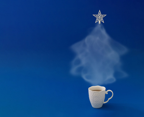 Christmas tree made of steaming coffee or tea with silver star on the top against blue background. Winter holiday concept. Minimal New Year background. Trendy Christmas idea. Copy space.
