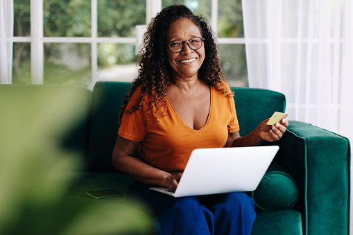 Mature woman enjoying her retirement by indulging in online shopping from the comfort of her home. Happy woman spending her leisure time browsing through ecommerce websites and ordering her favourite products.