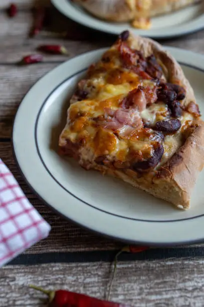 Delicious homemade tex mex pizza with kidney beans, bacon, cheddar cheese, red onions and tomatoes. Served sliced and ready to eat on a plate. Closeup, front view