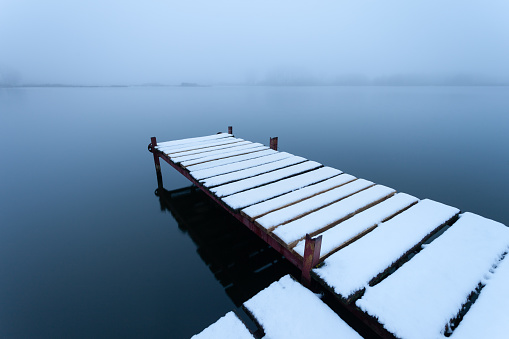Snow-covered pier on the lake on a foggy day, winter view in the eastern Poland