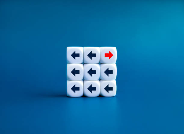 istock Leadership, opposite, disrupt, unique, think different way and stand out from the crowd concepts. Red go right and black go left, arrow direction symbol on white dice blocks on blue background. 1673996721