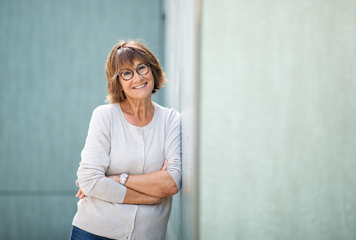 Portrait woman in 50s leaning against wall and smiling