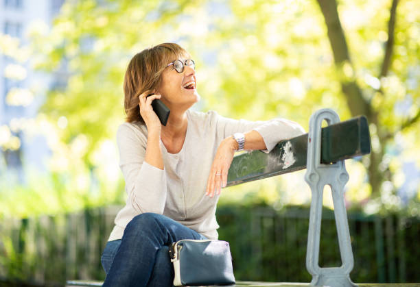 istock happy woman sitting on park bench talking with cellphone 1674014749