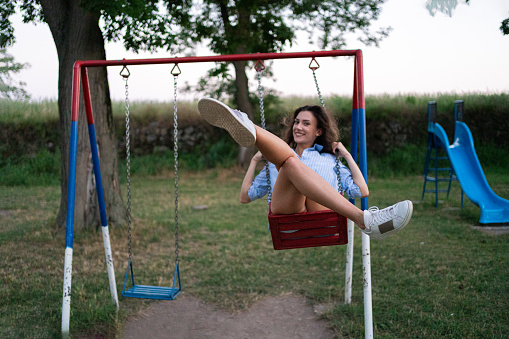 Portrait of carefree young Caucasian woman, swinging on a swing at the public park