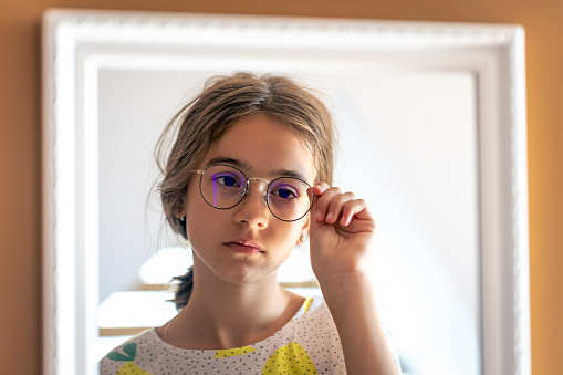 Sleepy teen girl in glasses looks at herself in the mirror in the morning, the concept of self-acceptance.