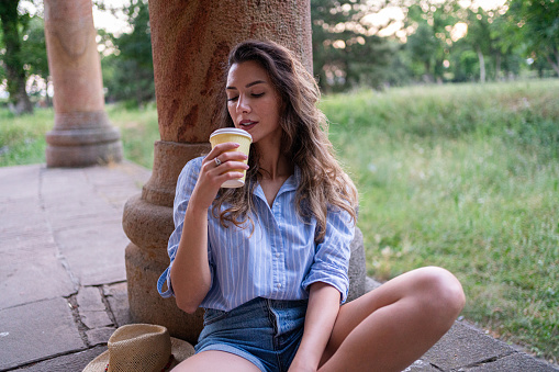 A young Caucasian woman, drinking coffee, while resting during a city exploration