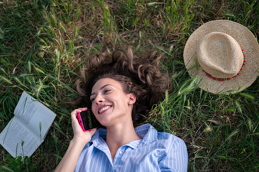 High angle view of an young Caucasian woman, talking on mobile phone while lying on the grass