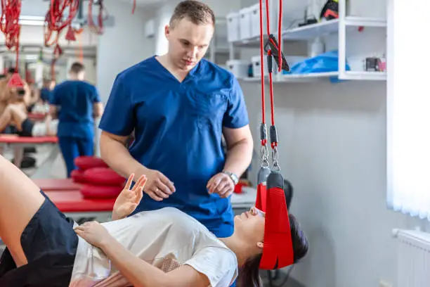 Photo of Female patient hanging on suspensions at rehabilitation center.