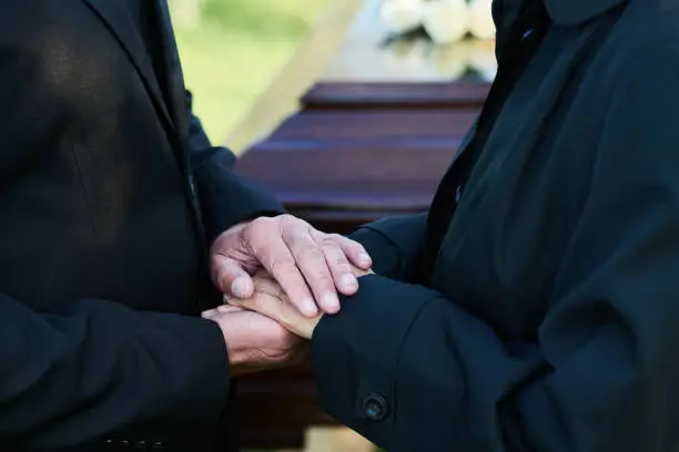 Photo of Close-up of hands of mature grieving man on those of his mourning wife