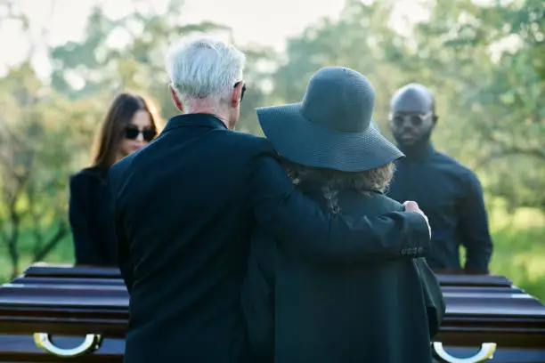 Photo of Rear view of mature grey haired man embracing his wife in black hat