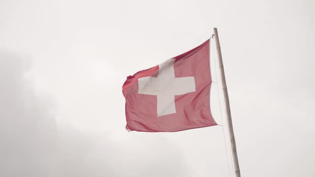 The Swiss Flag in the Pole Blown by the Wind with the Sky in the Background. Slow Motion