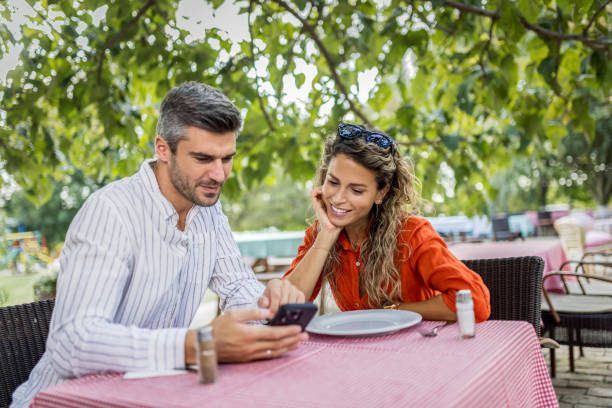 istock a young couple is using a mobile phone while having lunch and drinking wine 1674066264