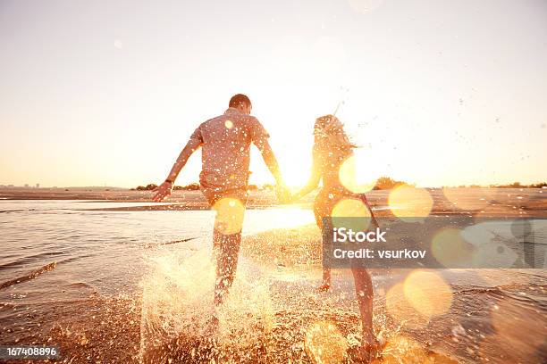 A Happy Couple Runs Through Waves On Sunlit Beach Stock Photo - Download Image Now - Couple - Relationship, Beach, Summer