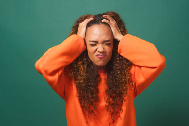 Frustrated and angry young woman 'tears hair out' - green studio background stock photo