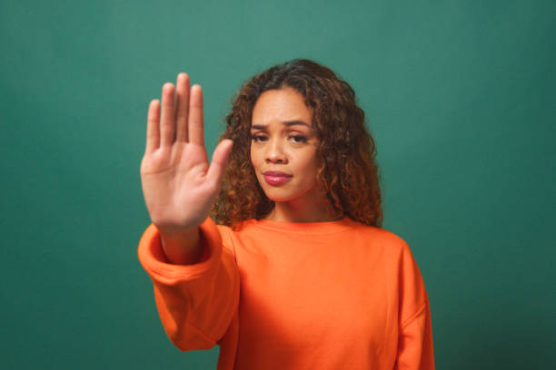 istock Young multi-ethnic woman holds up hand saying No, Stop, green studio background 1674089880