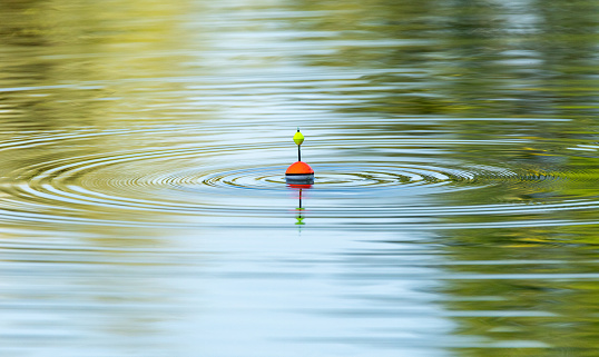 A fishing float floats on the water of the lake making circles in the water