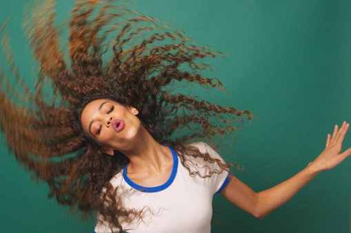 Young biracial woman dancing flipping hair, green studio background. High quality photo