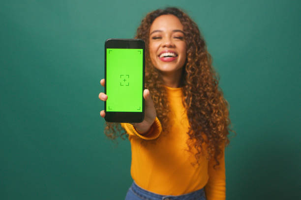 istock Happy young woman holds up device chroma key screen, green studio background 1674094627