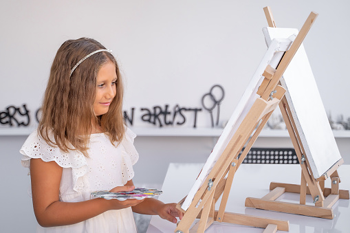 Girl At Art School Drawing Paint Acrylic Canvas and Easel in Art Class. Primary school kid learning how to draw and color