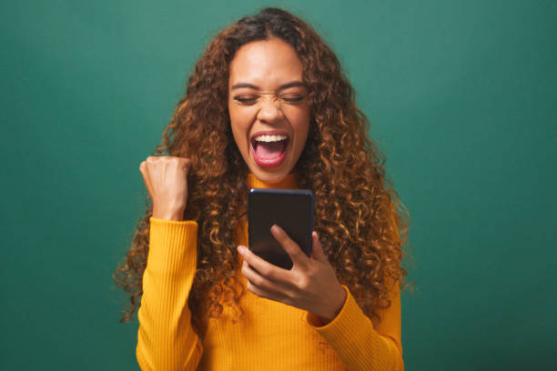 Young biracial woman cheers after reading text, green studio background